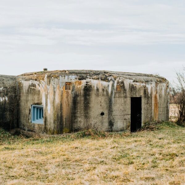 Wie viele Bunker hat Albanien? Faszinierende Fakten über das Land der Betonbunker Wie viele Bunker hat Albanien beschäftigt viele Reisende und Geschichtsinteressierte gleichermaßen. Schätzungen zufolge entstanden während der kommunistischen Herrschaft unter Enver Hoxha rund 170.000 bis über 200.000 Bunker, die bis heute das Landschaftsbild des Landes prägen. Von kleinen Betonkuppeln bis zu riesigen unterirdischen Anlagen erzählen die Bauwerke ein außergewöhnliches Kapitel der albanischen Geschichte. Warum so viele Bunker in Albanien errichtet wurden, welche Bedeutung sie heute haben und welche Anlagen besichtigt werden können, erfahren Sie in diesem Artikel. Wie viele Bunker hat Albanien? Schätzungen gehen davon aus, dass es in Albanien zwischen 170.000 und über 200.000 Bunker gibt. Genaue Zahlen existieren nicht, da viele Anlagen nie vollständig erfasst wurden oder im Laufe der Jahrzehnte zerstört beziehungsweise überbaut wurden. Fest steht jedoch, dass kaum ein anderes Land eine vergleichbare Dichte an Verteidigungsanlagen aufweist. Der überwiegende Teil der Bunker in Albanien entstand während der Herrschaft des kommunistischen Diktators Enver Hoxha zwischen den 1960er und 1980er Jahren. Kleine Betonbunker finden sich bis heute entlang der Küste, in den Bergen, auf Feldern und am Stadtrand. Viele stehen noch immer an ihrem ursprünglichen Standort und erinnern an eine Zeit, in der das Land aus Angst vor einer möglichen Invasion auf den Bau hunderttausender Schutzanlagen setzte. Warum hat Albanien so viele Bunker? Der Bau der zahlreichen Bunker in Albanien geht auf die Herrschaft des kommunistischen Diktators Enver Hoxha zurück. Während des Kalten Krieges verfolgte die Regierung eine Politik der Isolation und rechnete jederzeit mit einem möglichen Angriff durch ausländische Staaten. Aus dieser Paranoia heraus entstand eines der größten Bunkerbauprogramme Europas. Zu den wichtigsten Gründen für den massenhaften Bau gehörten: Angst vor einer möglichen Invasion aus dem Ausland. Abschottung Albaniens nach dem Bruch mit dem Warschauer Pakt. Wunsch, die gesamte Bevölkerung im Ernstfall verteidigen zu können. Errichtung kleiner Betonbunker in nahezu allen Landesteilen. Demonstration militärischer Stärke unter der Herrschaft von Enver Hoxha. Vorbereitung auf einen möglichen Angriff, obwohl es dafür keine konkreten Hinweise gab. Viele der Bauwerke wurden jedoch nie militärisch genutzt. Heute gelten sie als sichtbares Symbol für die kommunistische Vergangenheit Albaniens und erinnern an eine Epoche, die von politischer Kontrolle, Isolation und der ständigen Angst vor einer Bedrohung geprägt war. Bau der Bunker unter Enver Hoxha Der außergewöhnliche Umfang des Bunkerbaus lässt sich nur vor dem politischen Hintergrund der damaligen Zeit verstehen. Unter der Herrschaft von Enver Hoxha wurde der Ausbau der Verteidigungsanlagen zu einem zentralen Staatsprojekt, das das gesamte Land über viele Jahre hinweg prägte. Angst vor einer Invasion als Auslöser Unter Enver Hoxha herrschte die Überzeugung, dass Albanien jederzeit von einem fremden Staat angegriffen werden könnte. Spannungen während des Kalten Krieges, die zunehmende Isolation des Landes und der Austritt Albaniens aus dem Warschauer Pakt verstärkten die Sorge vor einer möglichen Invasion. Aus diesem Grund wurde der Schutz des Landes zu einer politischen Priorität. Ziel war es, für den Ernstfall in nahezu jeder Region Verteidigungsanlagen bereitzustellen. Bunker entstanden an Küsten, auf Feldern, in Gebirgen und in der Nähe wichtiger Verkehrswege. Auf diese Weise sollte ganz Albanien im Falle eines Angriffs verteidigt werden können. Massenproduktion aus Beton und Stahl Für den Bau der Bunker entwickelte die Regierung standardisierte Modelle, die in großer Stückzahl hergestellt wurden. Verwendet wurden vor allem Stahlbeton und massive Betonkuppeln, damit die Bauwerke möglichst widerstandsfähig waren. Viele der kleineren Anlagen bestanden aus mehreren Tonnen Beton und Stahl. Innerhalb weniger Jahre entstanden dadurch hunderttausende Bauwerke, die bis heute überall in der Landschaft zu finden sind. Nach dem Sturz des kommunistischen Regimes verloren die meisten Bunker ihre ursprüngliche Funktion. Einige wurden abgerissen oder umgewandelt, viele andere blieben als markantes Zeugnis der albanischen Geschichte erhalten. Bunker heute: Vom Verteidigungsbauwerk zur Sehenswürdigkeit Viele Bunker in Albanien haben ihre ursprüngliche militärische Funktion längst verloren. Stattdessen dienen einige heute als Museen, Ausstellungsräume oder beliebte Ausflugsziele. Andere stehen weiterhin verlassen in der Landschaft und erinnern an die Zeit der kommunistischen Herrschaft. Bunk'Art 1 und Bunk'Art 2 in Tirana Zu den bekanntesten Anlagen gehören Bunk'Art 1 und Bunk'Art 2 in Tirana. Beide ehemaligen Schutzbunker wurden in moderne Museen umgewandelt und vermitteln Besuchern einen umfassenden Einblick in die Geschichte Albaniens während der Diktatur von Enver Hoxha. Während Bunk'Art 1 am Fuße des Dajti-Gebirges als großer Atombunker entstand, widmet sich Bunk'Art 2 im Zentrum der Hauptstadt vor allem der Geschichte der Sigurimi, der albanischen Geheimpolizei. Beide Ausstellungen zählen heute zu den bekanntesten Sehenswürdigkeiten des Landes. Porto Palermo und weitere bekannte Bunker Auch Porto Palermo an der albanischen Riviera ist für seine militärischen Anlagen bekannt. Neben der historischen Festung befindet sich dort ein ehemaliger U-Boot-Bunker, der an die Verteidigungsstrategie während des Kalten Krieges erinnert und viele Besucher anzieht. Zahlreiche weitere Bunker finden sich entlang der Küste, rund um Durrës, bei Saranda oder am Stadtrand größerer Städte. Manche gelten als beliebte Lost Places, andere wurden zu Cafés, Unterkünften oder kleinen Ausstellungsräumen umgestaltet und zeigen, wie vielseitig die einstigen Verteidigungsanlagen heute genutzt werden können. Gibt es in Österreich noch Bunker? Auch in Österreich gibt es heute noch zahlreiche Bunker, allerdings deutlich weniger als in Albanien. Viele Anlagen stammen aus dem Zweiten Weltkrieg oder wurden während des Kalten Krieges errichtet. Ein Teil befindet sich weiterhin im Besitz des Bundesheeres, andere wurden stillgelegt oder einer neuen Nutzung zugeführt. Heute dienen einige Bunker als Museen, Lagerflächen oder technische Einrichtungen. Andere sind verschlossen oder stehen unter Denkmalschutz und können nur im Rahmen besonderer Führungen besichtigt werden. Im Vergleich zu Albanien, wo noch zehntausende kleine Betonbunker das Landschaftsbild prägen, sind Bunkeranlagen in Österreich deutlich seltener und meist auf einzelne Standorte konzentriert. Welcher ist der größte Bunker in Albanien? Als größter Bunker in Albanien gilt der ehemalige Atombunker in Tirana, der heute als Bunk'Art 1 bekannt ist. Die weitläufige unterirdische Anlage wurde für die politische und militärische Führung des Landes errichtet und sollte im Falle eines Angriffs als geschützter Rückzugsort dienen. Heute ist der Bunker als Museum für Besucher geöffnet. Zu den größten und bekanntesten Bunkeranlagen gehören außerdem: Bunk'Art 1 am Fuße des Dajti bei Tirana mit zahlreichen unterirdischen Räumen. Bunk'Art 2 im Zentrum der Hauptstadt, das sich der Geschichte der Sigurimi widmet. Der ehemalige U-Boot-Bunker von Porto Palermo an der albanischen Riviera. Große militärische Anlagen im Raum Durrës, die einst Teil des Verteidigungssystems waren. Viele dieser Bauwerke entstanden während der Herrschaft von Enver Hoxha und zählen heute zu den bedeutendsten Erinnerungsorten des Landes. Sie vermitteln einen eindrucksvollen Einblick in die Geschichte Albaniens und zeigen, welchen Stellenwert der Bunkerbau während des Kalten Krieges hatte. Welches Land hat die meisten Bunker in Europa? Welche Nation als Land mit den meisten Bunkern in Europa gilt, hängt von der jeweiligen Definition ab. Betrachtet man private und öffentliche Schutzräume, liegt die Schweiz mit rund 370.000 Anlagen vorn. Dort stehen etwa neun Millionen Schutzplätze zur Verfügung, sodass im Ernstfall rechnerisch die gesamte Bevölkerung untergebracht werden könnte. Albanien ist dagegen für seine besonders hohe Dichte an militärischen Betonbunkern bekannt. Während der Herrschaft von Enver Hoxha entstanden schätzungsweise rund 170.000 bis 200.000 Bunker, wobei ältere Angaben teils deutlich höhere Zahlen nennen. Im Verhältnis zur Fläche prägen diese Bauwerke das Land stärker als in fast jedem anderen europäischen Staat. Damit gilt Albanien vor allem als Europas bekanntestes Land mit Bunkern, während die Schweiz zahlenmäßig mehr Schutzräume besitzt. Fazit: Wie viele Bunker hat Albanien? Genaue Zahlen gibt es bis heute nicht, doch Schätzungen gehen von 170.000 bis über 200.000 Bunkern aus. Kaum ein anderes Land in Europa wurde durch ein vergleichbares Verteidigungsprogramm so stark geprägt. Viele der markanten Betonkuppeln sind noch immer fester Bestandteil des Landschaftsbildes. Heute stehen zahlreiche Bunker in Albanien als Erinnerung an die kommunistische Vergangenheit. Während einige Anlagen zu Museen oder Sehenswürdigkeiten umgestaltet wurden, liegen andere weiterhin verlassen in der Natur. Gerade dieser außergewöhnliche Mix aus Geschichte, Architektur und Zeitzeugen macht die albanischen Bunker bis heute zu einem besonderen Merkmal des Landes. FAQs: "Wie viele Bunker hat Albanien" Wie unterscheiden sich die verschiedenen Bunkertypen in Albanien? Bunkertyp Verwendung Kleine Kuppelbunker Schutz einzelner Soldaten Mittlere Bunker Unterkünfte und Verteidigungsstellungen Große unterirdische Anlagen Führungseinrichtungen und Schutzbunker für Militär und Regierung U-Boot-Bunker Militärische Nutzung an der Küste Kann man verlassene Bunker auf eigene Faust besuchen? Grundsätzlich ja, allerdings sollte dabei Vorsicht gelten. Nur offiziell zugängliche Anlagen betreten. Sperrungen und Warnhinweise beachten. Festes Schuhwerk tragen. Taschenlampe für dunkle Bereiche mitnehmen. Abgelegene Bunker möglichst nicht allein besuchen. Werden in Albanien heute noch neue Bunker gebaut? Nein. Mit dem Ende der kommunistischen Herrschaft wurde der Bau neuer Bunkeranlagen eingestellt. Stattdessen werden bestehende Bauwerke erhalten, umgenutzt oder schrittweise zurückgebaut. Warum stehen viele Bunker direkt an Stränden und Küsten? Während des Kalten Krieges galt besonders die Küste als möglicher Angriffspunkt. Deshalb entstanden entlang des Meeres zahlreiche Verteidigungsanlagen, die eine Landung feindlicher Truppen erschweren sollten. Kann man in Albanien in einem Bunker übernachten? wie viele bunker hat albanien